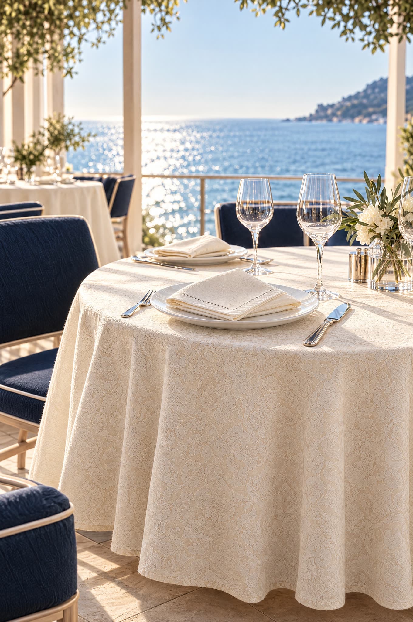 Table de restaurant dressée d'une nappe jacquard et de serviettes ivoire face à la mer